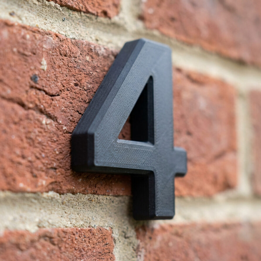 Zwart kunststof huisnummer 4 bevestigd op een bakstenen muur, strak en modern ontwerp