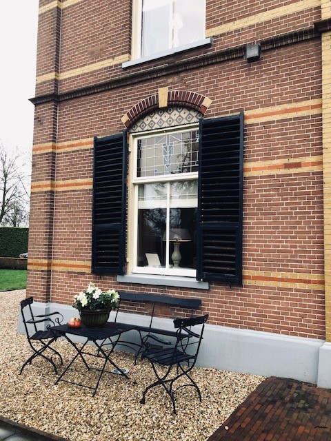 Buitenraam met mat plexiglas en zwarte luiken bij een woonhuis