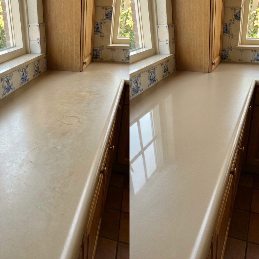 Licht stenen keukenblad bij een raam, schoon en leeg, met daglicht dat op het oppervlak valt.