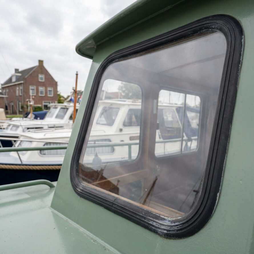 Kunststof raam met groen frame, gezien vanaf de binnenzijde van een boot in de haven.
