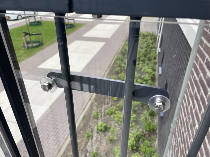 Close-up van een glasbevestiging aan een metalen balustrade met klem en bout.