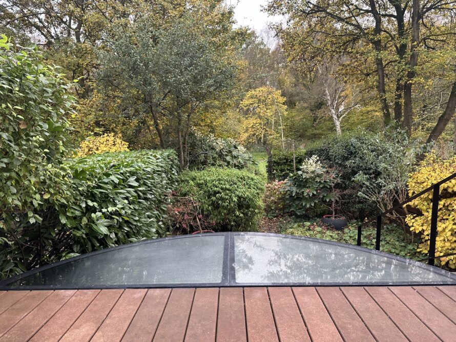 Gebogen plexiglas serre aan een terras met uitzicht op een groene tuin.