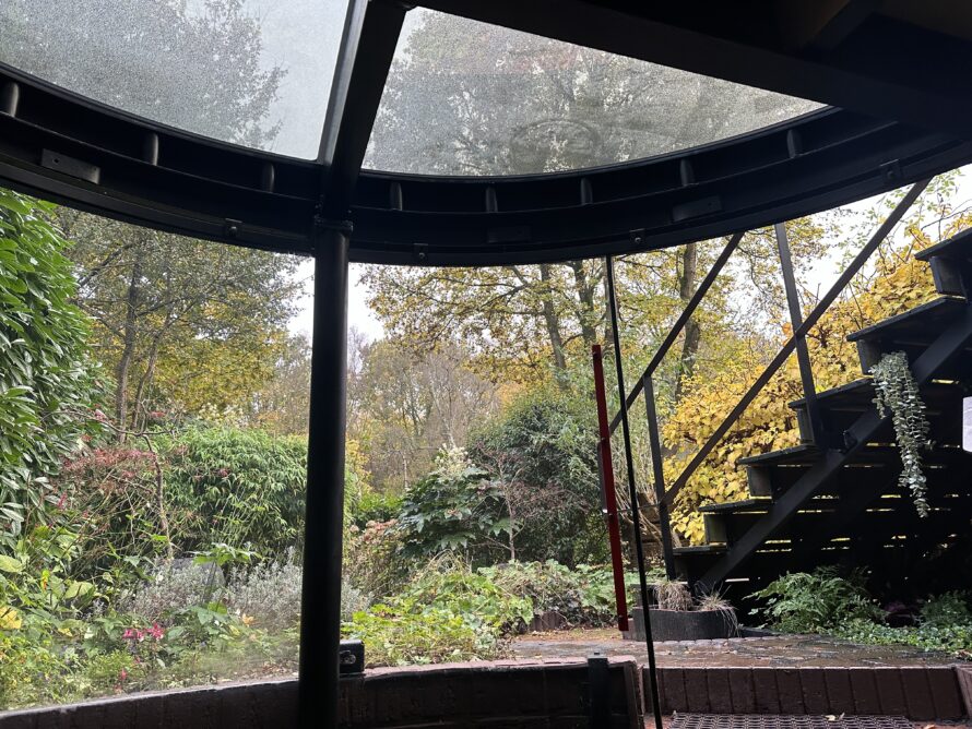 Interieur van een gebogen plexiglas serre met transparant dak en uitzicht op de tuin