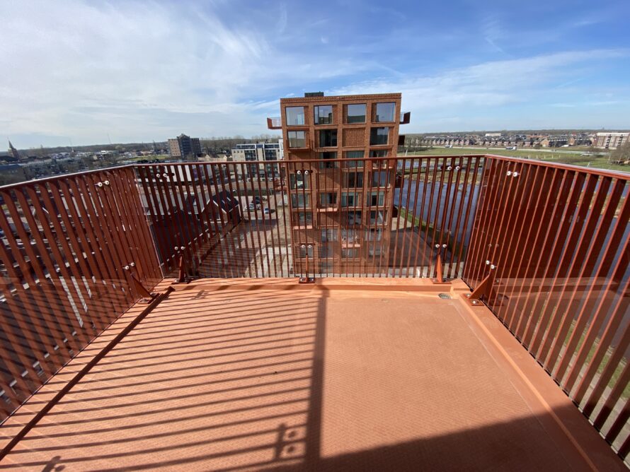 Uitzichtplatform met roestkleurige metalen railing en uitzicht over water en landschap.