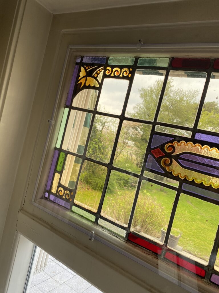 Glas-in-loodraam met decoratieve rand en uitzicht op groen buiten.