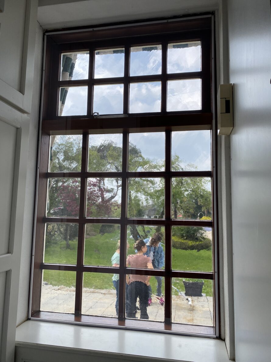 Groot raam met houten roedeverdeling en uitzicht op groene tuin.