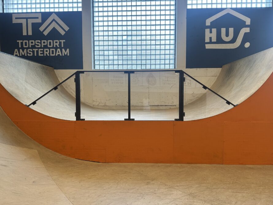 Overdekte skatekom met houten afwerking, zwarte reling bovenop en oranje bekleding aan de onderzijde.