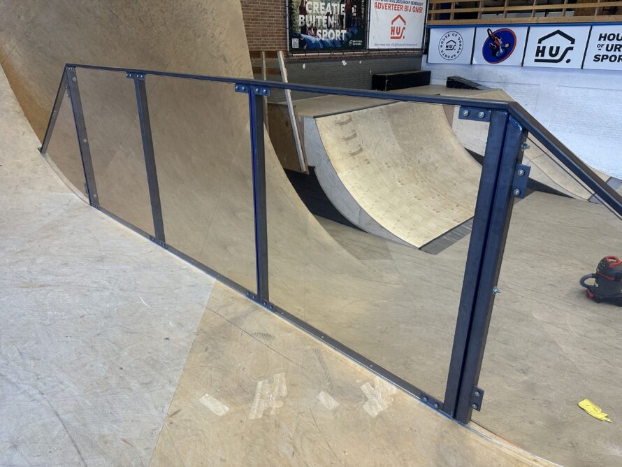 Transparante polycarbonaat panelen gemonteerd in blauwe stalen frames langs een gebogen skate ramp.